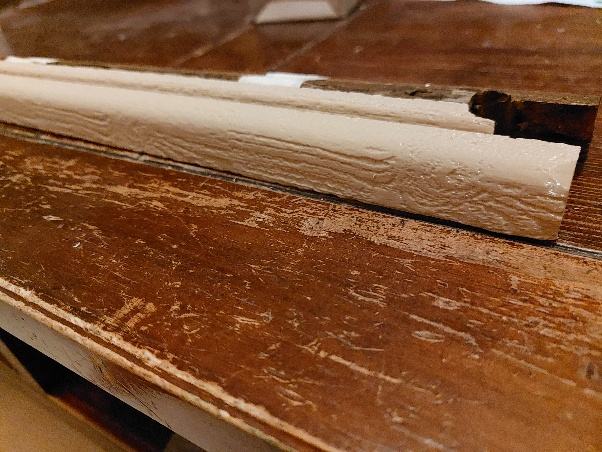 Moulure reproduite en impression 3D, veinage bois imité, posée contre l’encadrement de fenêtre d’origine